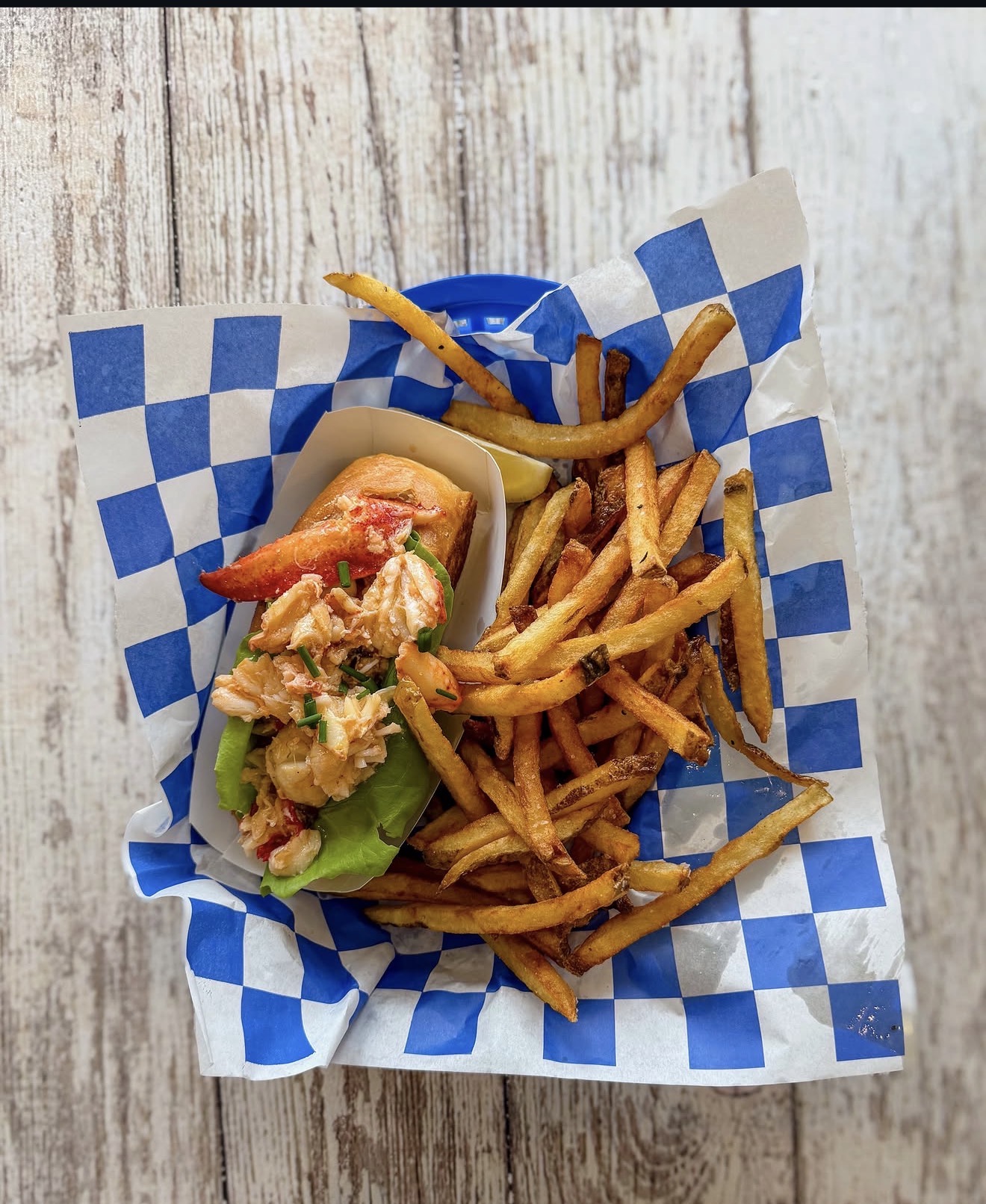Close-up of a Maine lobster roll loaded with claw and tail meat, chives, lettuce, and lemon wedge on a toasted bun